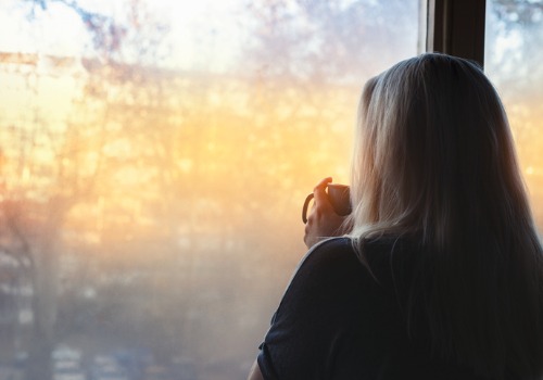 A depressed woman looking out the window, needing therapy through Telehealth in Peoria IL